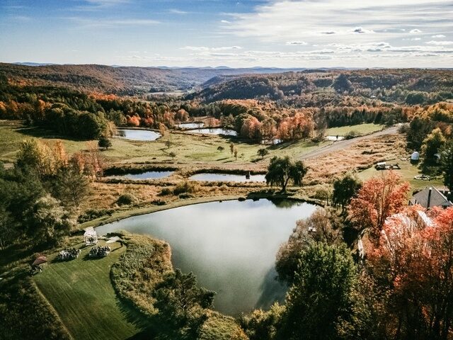 Wide aerial view of the Twelve Ponds property in fall, ponds cascading down the valley toward the Catskills.