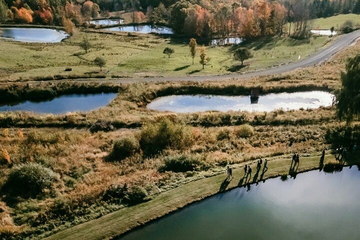 Aerial view of guests gathered by a pond at Twelve Ponds in fall, additional ponds visible beyond.