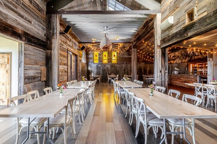 The barn at Twelve Ponds set for dinner, harvest tables, cross-back chairs and string lights.