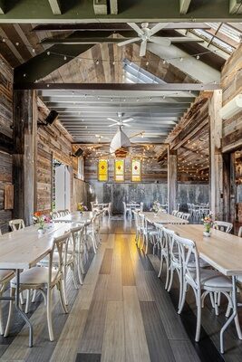 Interior of the barn at Twelve Ponds set for a dinner, cathedral ceiling and hanging string lights.