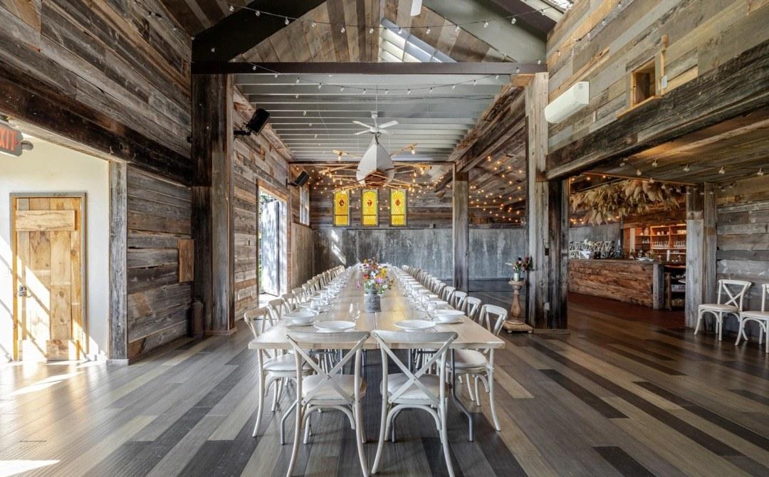 Long dining table set in the rustic barn at Twelve Ponds, surrounded by reclaimed wood walls and string lights.