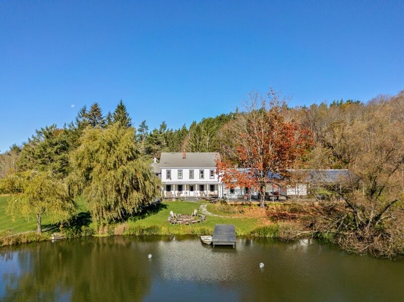 The farmhouse at Twelve Ponds seen across a pond, willow tree and autumn foliage reflected in the water.