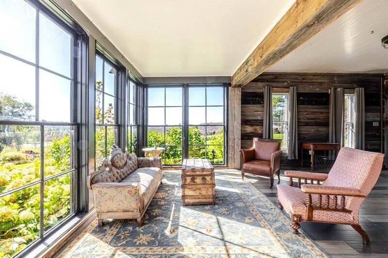 Sunroom at Twelve Ponds with tall windows, antique settee and rug looking over the fields.